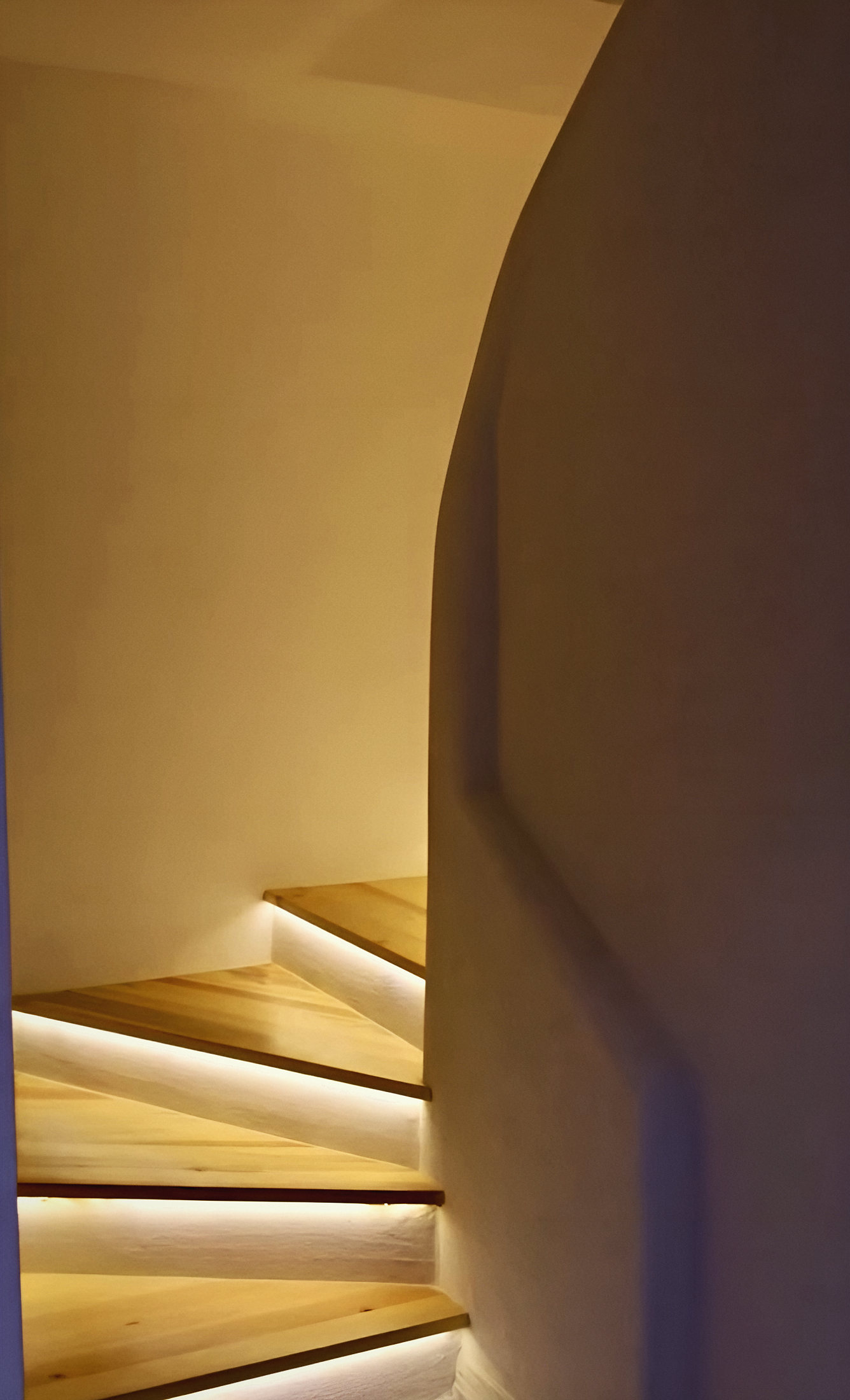 A curving plastered stair with softly lit oak treads